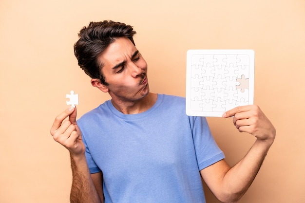 Young caucasian man holding a puzzle isolated on beige background