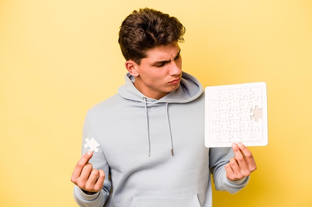 Young caucasian man holding puzzle isolated on yellow background