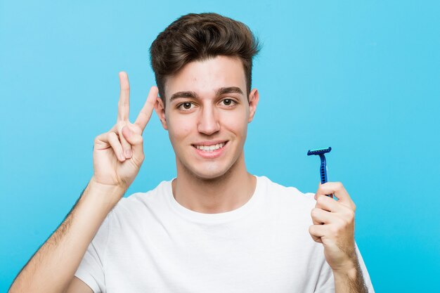 Giovane uomo caucasico che tiene una lametta che mostra il segno di vittoria e che sorride ampiamente.