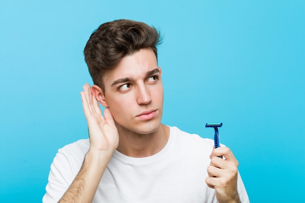 Young caucasian man holding a razor blade trying to listening a gossip.