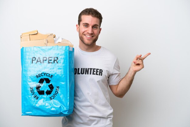 Young caucasian man holding a recycling bag full of paper to recycle isolated on white background pointing finger to the side