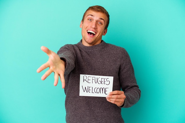 Photo young caucasian man holding a refugees welcome placard isolated on blue background