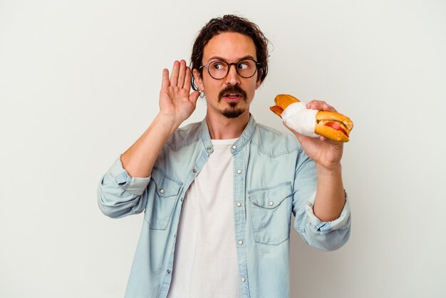 Young caucasian man holding a sandwich   trying to listening a gossip.