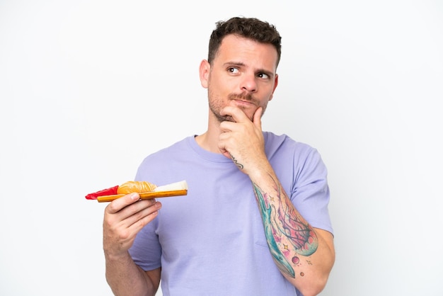 Young caucasian man holding sashimi isolated on white background having doubts and thinking