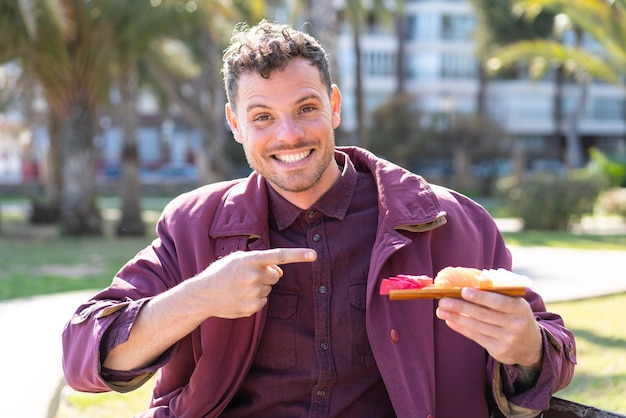 Young caucasian man holding sashimi at outdoors and pointing it