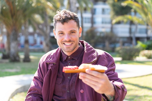 Photo young caucasian man holding sashimi at outdoors with happy expression