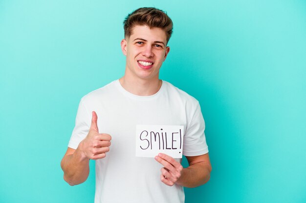 Young caucasian man holding a smile placard isolated on blue background