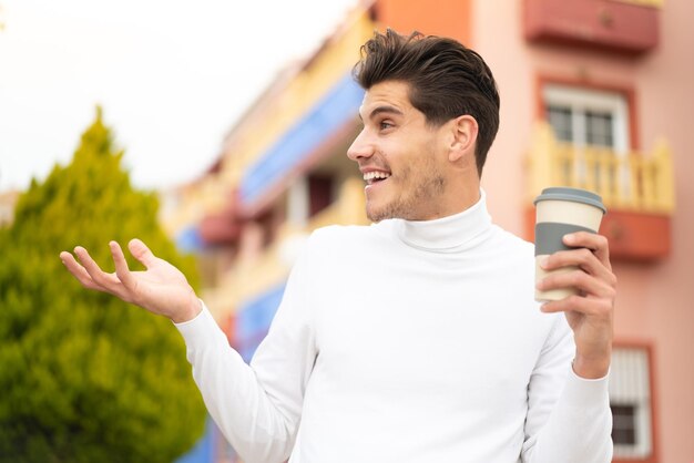 Young caucasian man holding a take away coffee at outdoors with surprise facial expression