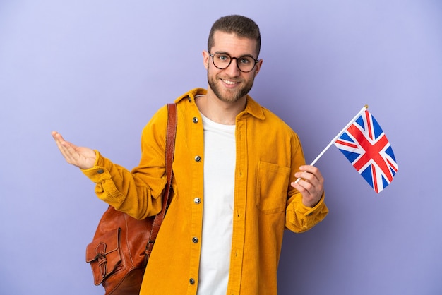 Young caucasian man holding an United Kingdom flag isolated on purple extending hands to the side for inviting to come