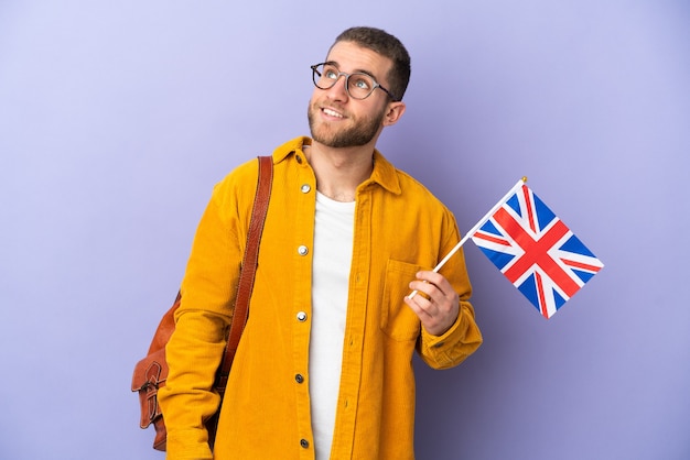 Young caucasian man holding an United Kingdom flag isolated on purple wall thinking an idea while looking up