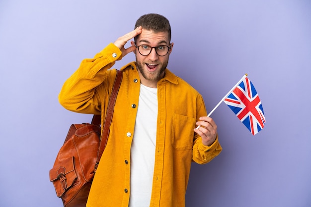 Young caucasian man holding an United Kingdom flag isolated on purple wall with surprise expression
