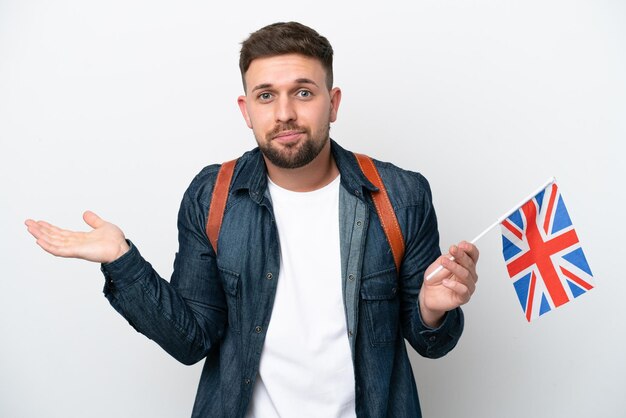 Young caucasian man holding an United Kingdom flag isolated on white background having doubts while raising hands