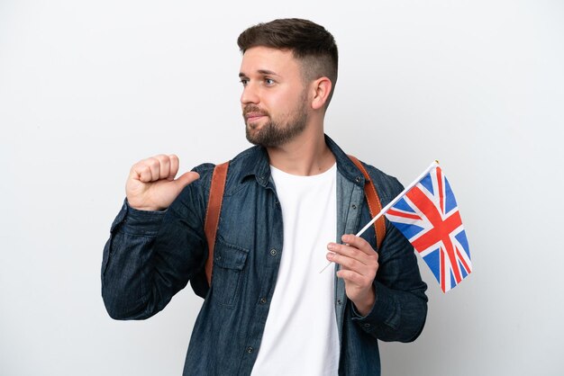 Young caucasian man holding an United Kingdom flag isolated on white background proud and selfsatisfied