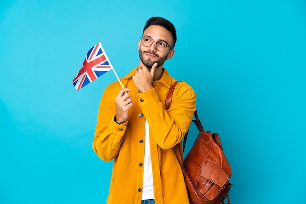 Young caucasian man holding an United Kingdom flag isolated on yellow wall and looking up