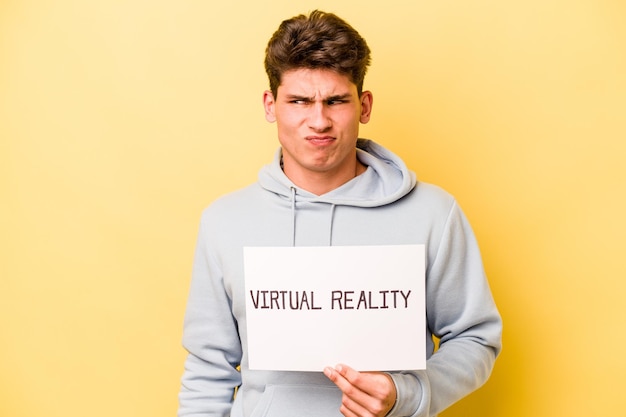 Young caucasian man holding virtual placard isolated on yellow background confused feels doubtful and unsure