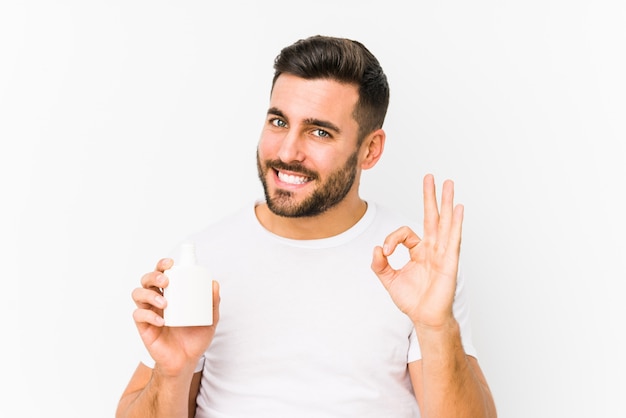 Young caucasian man holding a vitamins bottle cheerful and confident showing ok gesture.