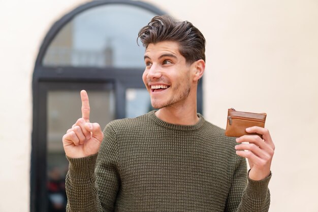 Young caucasian man holding a wallet at outdoors intending to realizes the solution while lifting a finger up