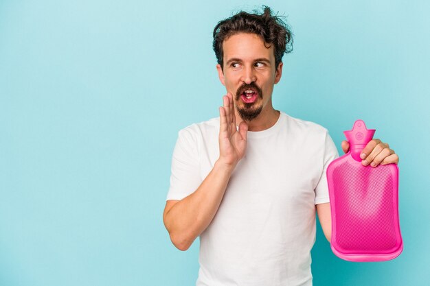 Young caucasian man holding a water bag isolated on blue background is saying a secret hot braking news and looking aside