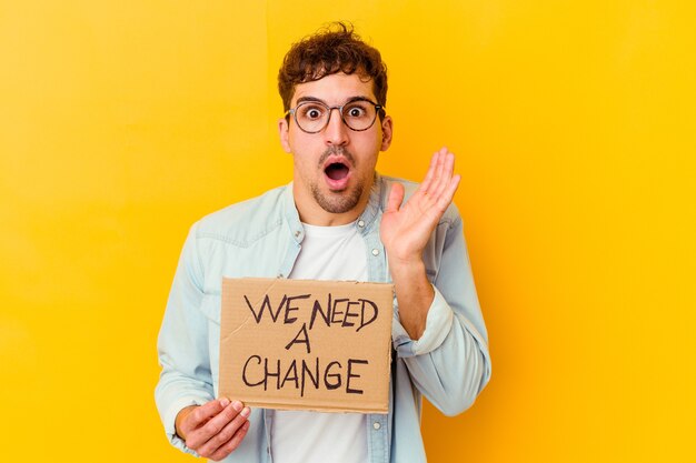 Young caucasian man holding a we need a change placard isolated surprised and shocked