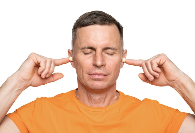 Young caucasian man inserting earplugs into his ears over white background