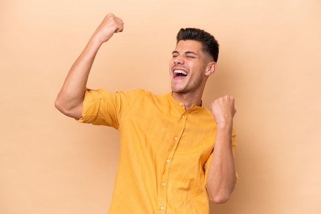 Young caucasian man isolated on beige background celebrating a victory