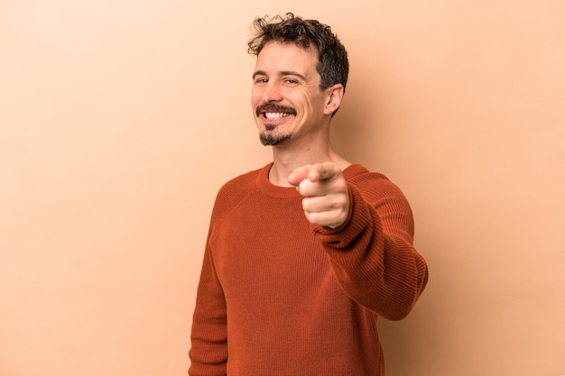 Young caucasian man isolated on beige background cheerful smiles pointing to front.