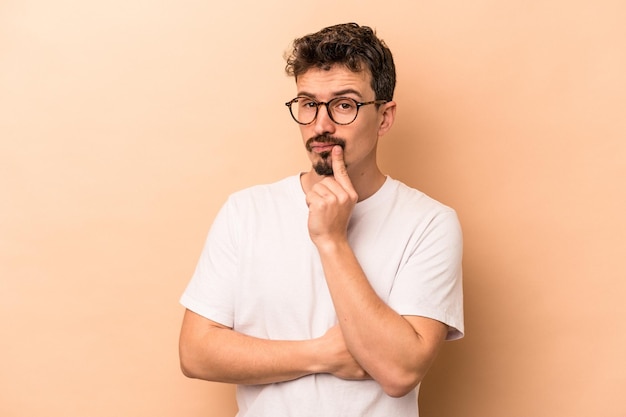 Young caucasian man isolated on beige background contemplating, planning a strategy, thinking about the way of a business.