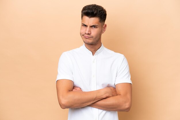 Young caucasian man isolated on beige background feeling upset