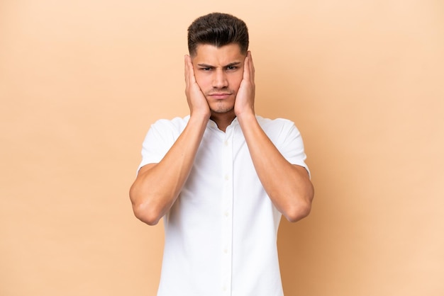 Young caucasian man isolated on beige background frustrated and covering ears