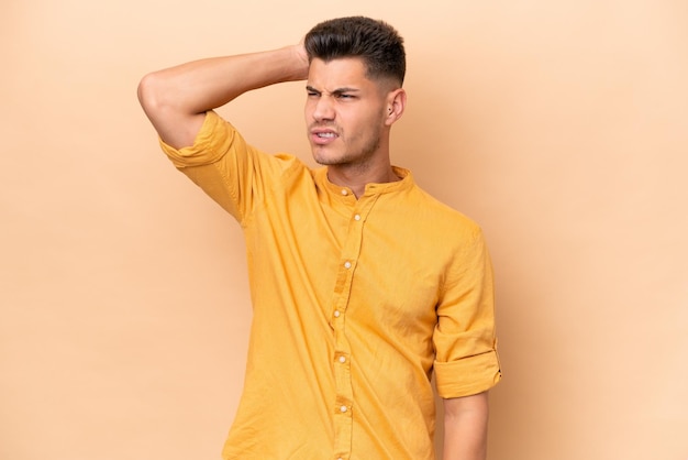 Young caucasian man isolated on beige background having doubts while scratching head