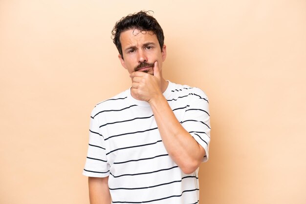 Young caucasian man isolated on beige background having doubts