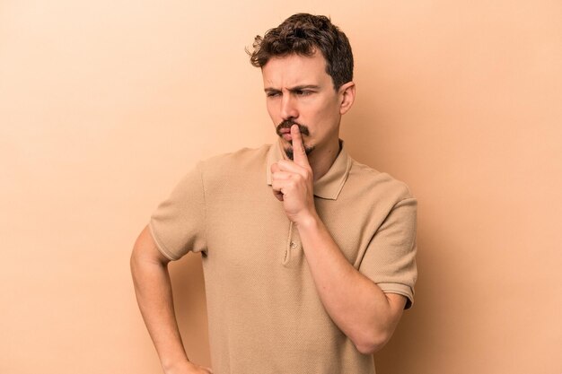 Young caucasian man isolated on beige background keeping a secret or asking for silence.