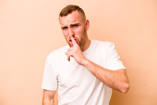 Young caucasian man isolated on beige background keeping a secret or asking for silence