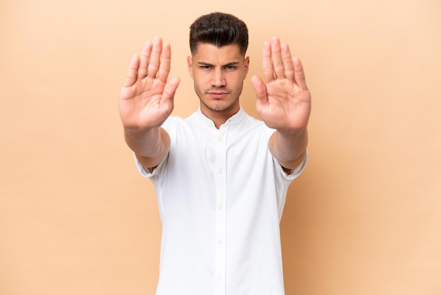 Young caucasian man isolated on beige background making stop gesture and disappointed