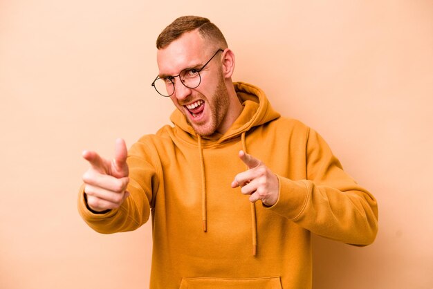 Young caucasian man isolated on beige background pointing to front with fingers