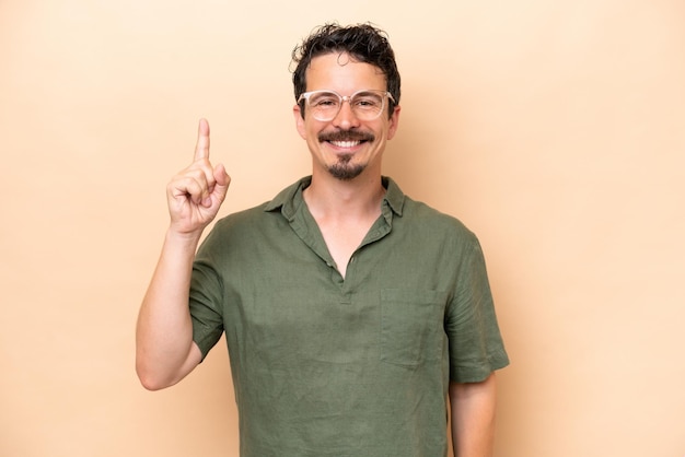 Young caucasian man isolated on beige background pointing up a great idea