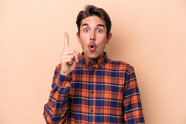 Young caucasian man isolated on beige background pointing upside with opened mouth.