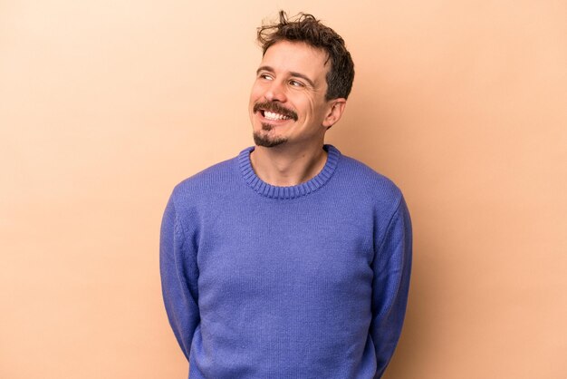 Young caucasian man isolated on beige background relaxed and happy laughing, neck stretched showing teeth.