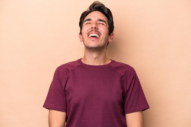 Young caucasian man isolated on beige background relaxed and happy laughing neck stretched showing teeth