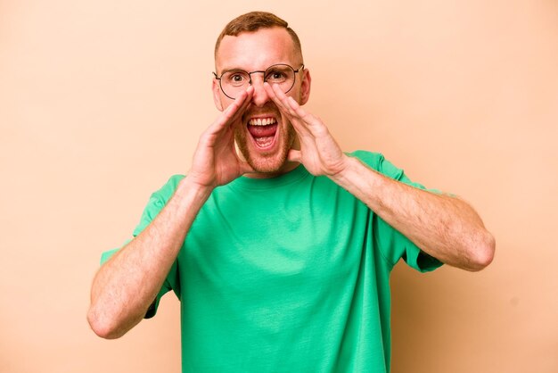 Young caucasian man isolated on beige background saying a gossip pointing to side reporting something