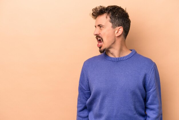 Young caucasian man isolated on beige background shouting very angry rage concept frustrated