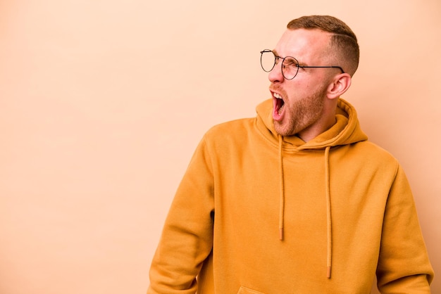 Young caucasian man isolated on beige background shouting very angry rage concept frustrated