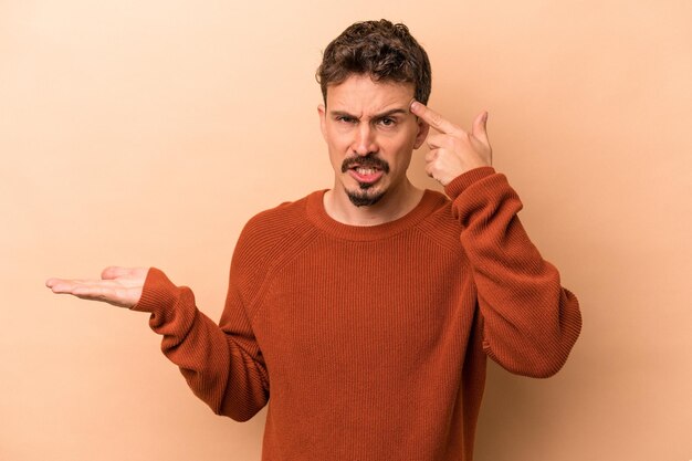 Young caucasian man isolated on beige background showing a disappointment gesture with forefinger.