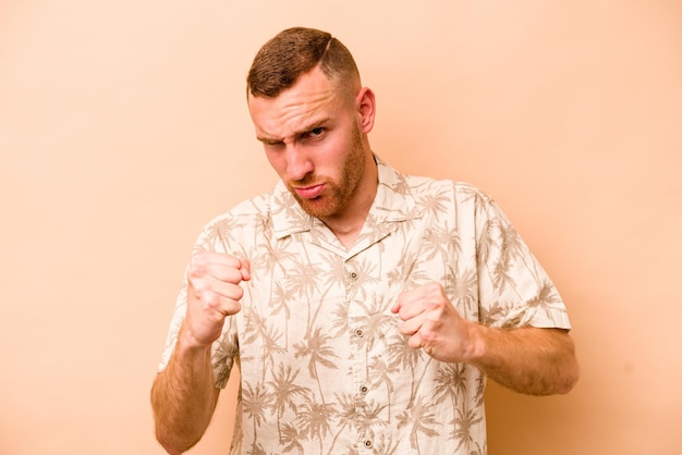 Young caucasian man isolated on beige background showing fist to camera aggressive facial expression