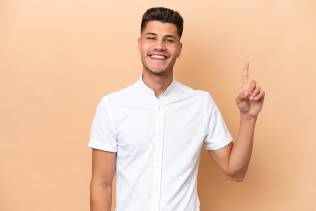 Young caucasian man isolated on beige background showing and lifting a finger in sign of the best