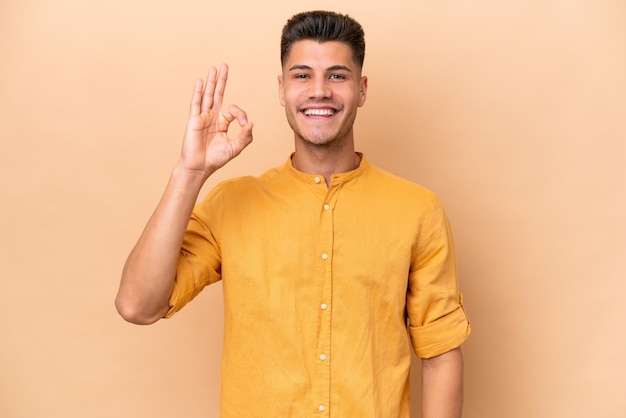 Young caucasian man isolated on beige background showing ok sign with fingers