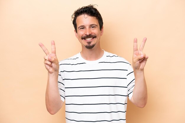 Young caucasian man isolated on beige background showing victory sign with both hands