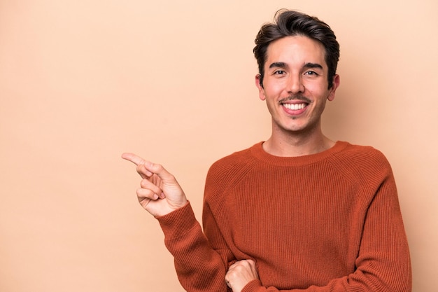 Young caucasian man isolated on beige background smiling cheerfully pointing with forefinger away.