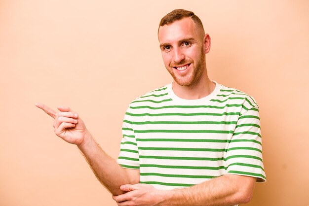 Young caucasian man isolated on beige background smiling cheerfully pointing with forefinger away