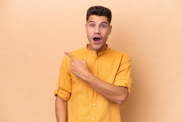 Young caucasian man isolated on beige background surprised and pointing side